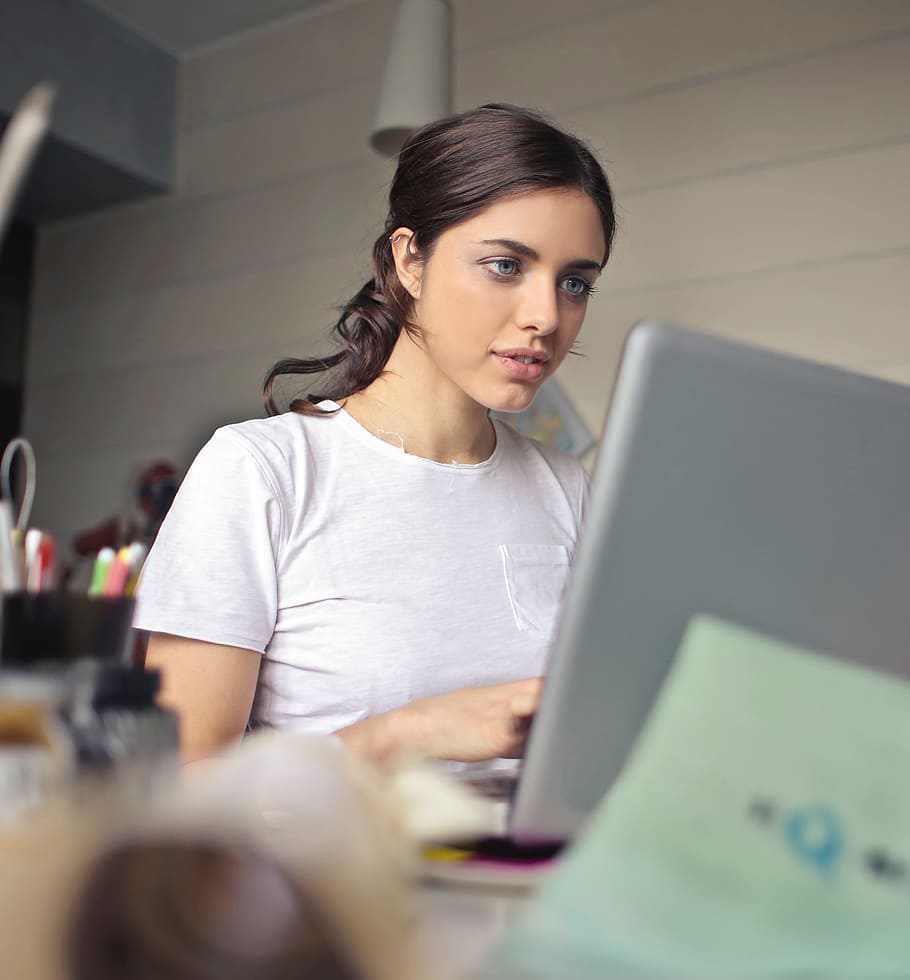 young, brunette, woman, wearing, white, t-shirt, working, laptop, looking, pen