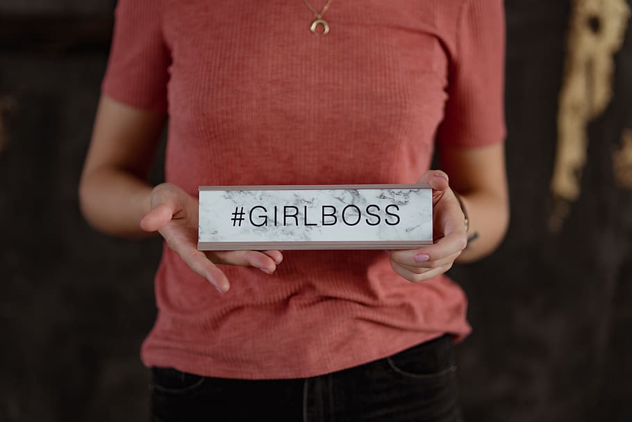 young, woman, holding, girlboss desk sign, girlboss, businesswoman, desk sign, girl, female, caucasian