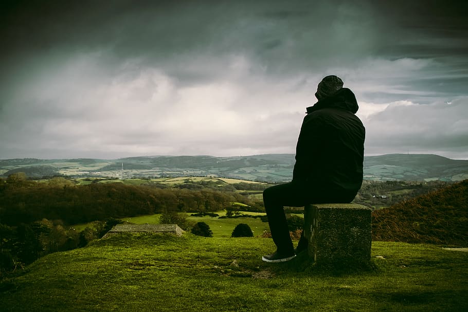 homem, desfrutando, paisagem, sentado, rocha, dramático, nuvens, escuro, verde, grama