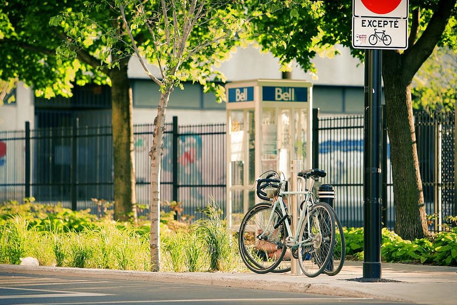 bikes, bicycles, street, pavement, sidewalk, trees, grass, bushes, posts, telephone booth