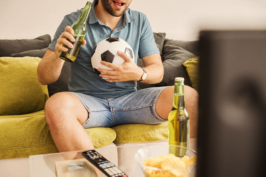 jovem, homem, assistindo, futebol, tv, bebendo cerveja, casa, sofá, exploração, sala de estar