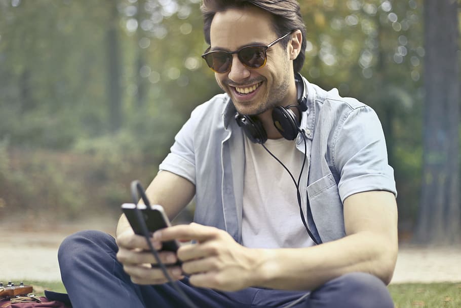 Hombre, vistiendo, teléfono inteligente, 25-30 años, escuchando, música, viejo, al aire libre, parque, gafas de sol