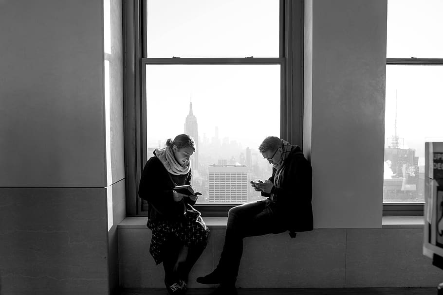 man and woman, sitting, window, couple, view, black and white, skyline, reading, mobile phone, real people
