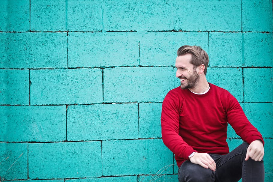adult man, wearing, red, sweater, leaning, turquoise, brick wall, 30-35 years old, Adult, Outdoors