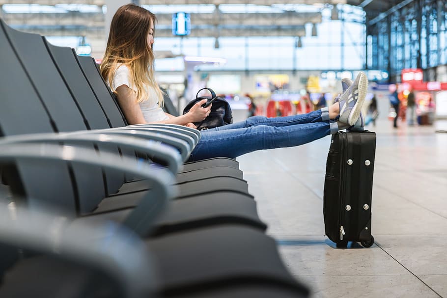 young, girl, long, hair, sitting, airport., put, legs, suitcase, near.