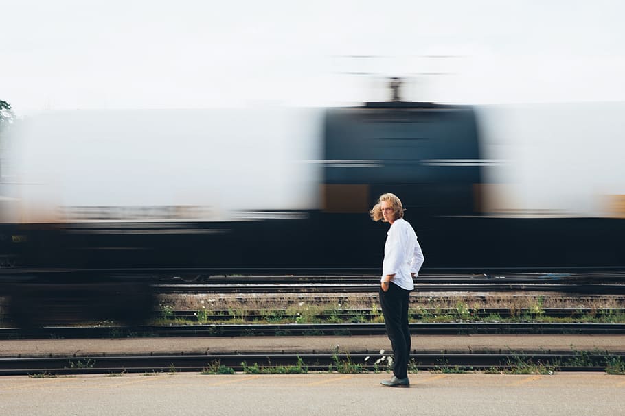long, haired, young, caucasian man, standing, passing, train, 20-25 year old, blur, hand in pocket