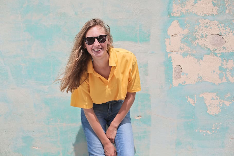 young, woman, wearing, yellow, polo shirt, sunglasses, standing, front, teal, concrete